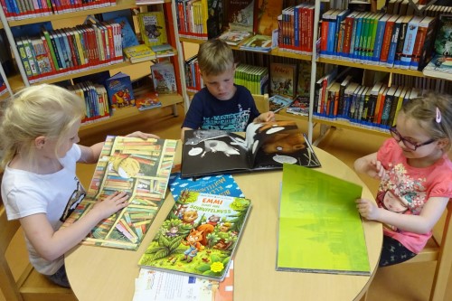 3 Kinder sitzen in der Bibliothek an einem Tisch und lesen