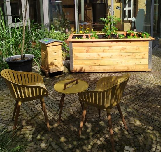 eine Bienenbeute steht neben einem Hochbeet in einem Innenhof
