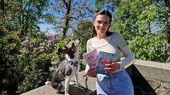 Eine junge Frau mit einem Hund. Die Frau hält bücher in der Hand.