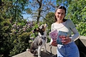 Eine junge Frau mit einem Hund. Die Frau hält bücher in der Hand.