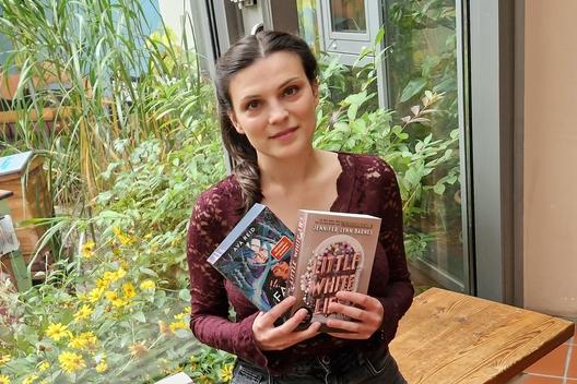 eine junge Frau sitzt auf einer Bank in der Bibliothek und hält zwei Bücher in den Händen