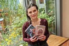 eine junge Frau sitzt auf einer Bank in der Bibliothek und hält zwei Bücher in den Händen